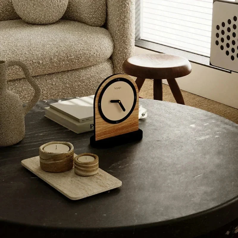 Wooden clock on a table with a couch and stool in the background
