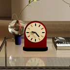 Red clock with colorful numbers on a table next to a plant and books