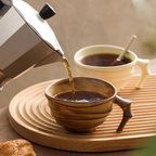 Coffee being poured from a pot into a ceramic cup on a wooden tray.