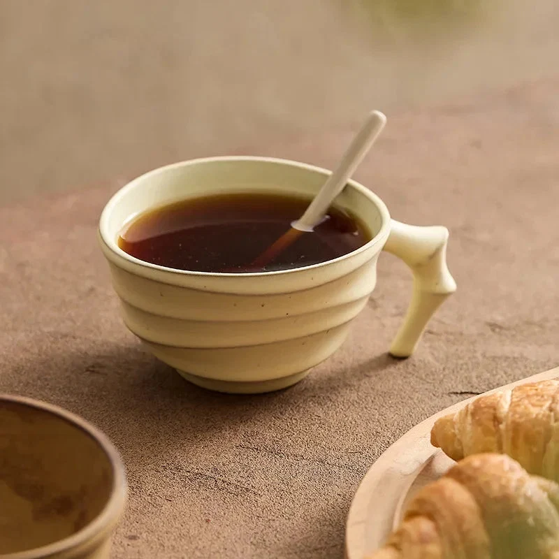 Ceramic mug with a handle filled with a dark liquid, possibly coffee, on a textured surface with a croissant.