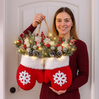 Person holding a decorative hanging with red mittens and Christmas elements against a white door.