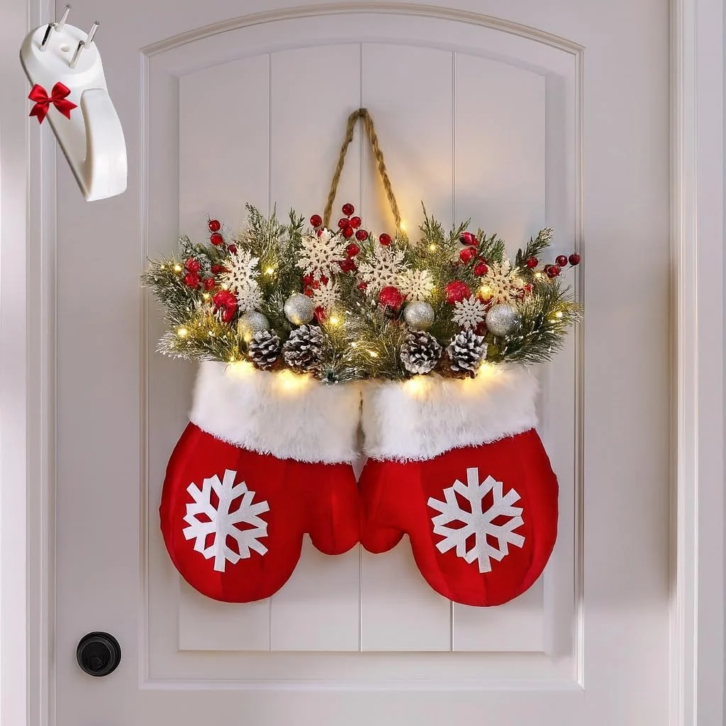 A festive Christmas wreath hanging on a white paneled door, featuring two red knit stocking shapes with white snowflake patterns, white faux fur trim, green pine branches, red berries, pinecones, and warm string lights. A small white ornament with a red bow is shown floating in the upper left corner.
