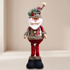 A plush Christmas Santa doll standing upright, wearing a red and gray plaid outfit, white beard, dark boots, and a decorated hat, photographed against a plain beige indoor backdrop.