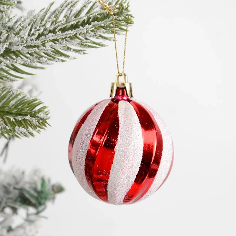A red and white striped Christmas ornament with glittery white stripes, hanging from a gold string near frosted green pine branches against a white background.