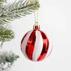 A red and white striped Christmas ornament with glittery white stripes, hanging from a gold string near frosted green pine branches against a white background.