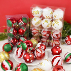 A set of Christmas ball ornaments in clear plastic packaging and scattered on a white surface, featuring red, white, and green designs with gold accents, set against a solid red background with green pine branches.