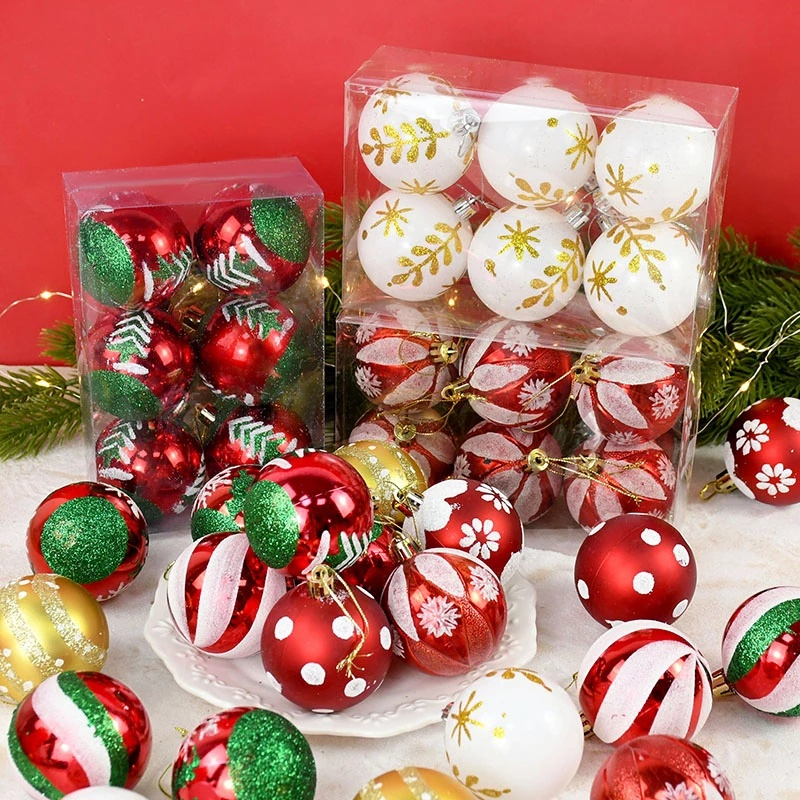 A set of Christmas ball ornaments in clear plastic packaging and scattered on a white surface, featuring red, white, and green designs with gold accents, set against a solid red background with green pine branches.