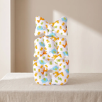 A baby support pillow with a dinosaur and elephant pattern, styled in a stacked position on a beige fabric-covered table against a neutral beige wall.