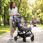 A woman pushes a baby stroller on a paved path in a sunlit park. The stroller has a dark gray and black frame with a gray star-patterned seat cover and matching headrest cushion, and a baby is seated inside.