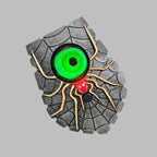 A Halloween-style spider eye wall decor piece featuring a textured gray spiderweb design, a large glowing green eye, gold-toned spider legs, and a small red light at the center, shown on a plain gray background.