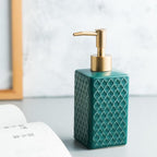 Teal soap dispenser with gold pump on a light surface