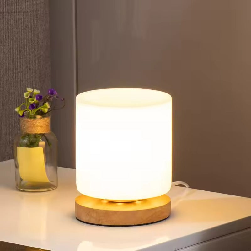 Table lamp with wooden base on a surface next to a vase with flowers, against a neutral background