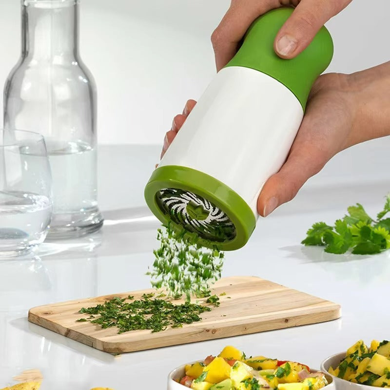 Hand using a green and white herb grinder to sprinkle herbs onto a wooden cutting board.