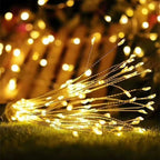 Warm white LED fairy string lights draped across green grass, with glowing bokeh lights in the background.