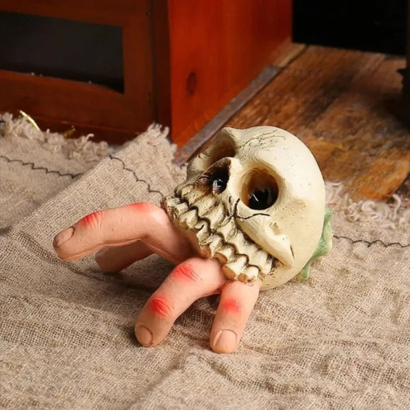 Skull-shaped object held by a hand with red nail polish on a textured surface.
