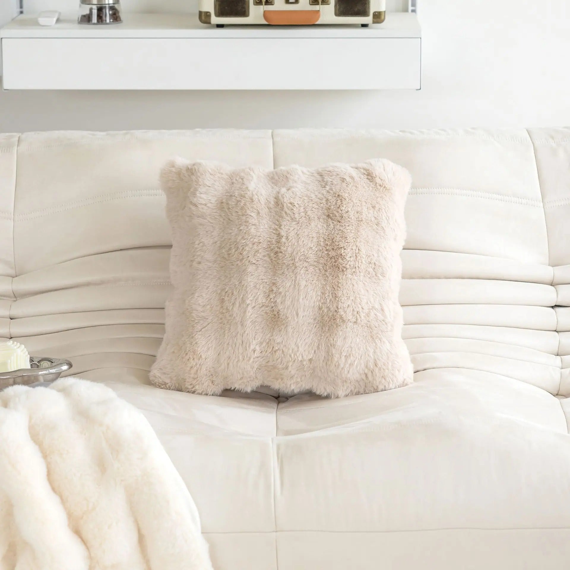 Beige pillow on a white couch with a white blanket