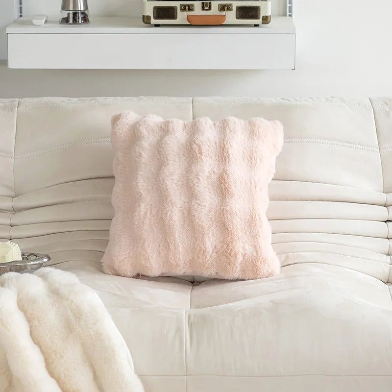 Pink textured pillow on a white couch with a white wall and shelf in the background.