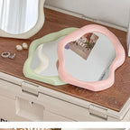 Heart-shaped mirrors in pink and green on a wooden surface with jewelry.