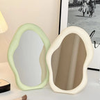 Two unique-shaped mirrors in green and white on a surface with a blurred background.