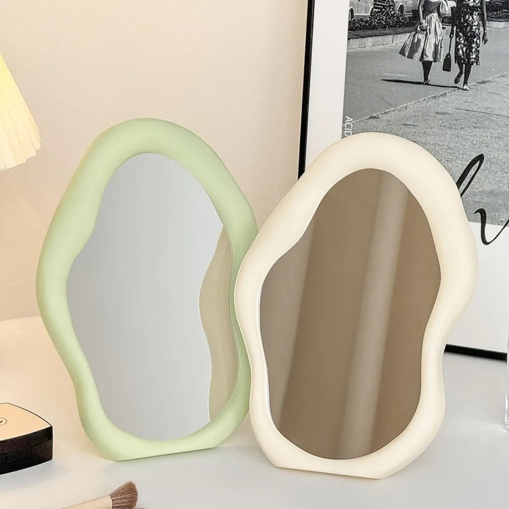 Two unique-shaped mirrors in green and white on a surface with a blurred background.