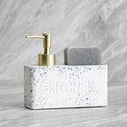 White terrazzo kitchen sink caddy with gold pump and gray sponge on a marble background