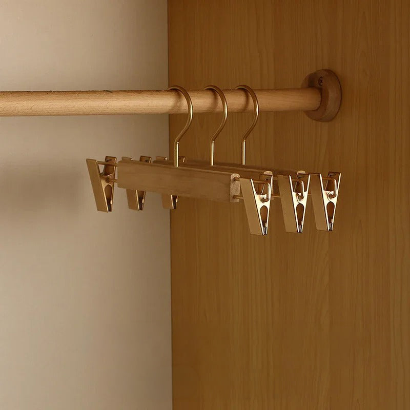 A wooden closet rod organizer with metal hangers and clips mounted on a wooden wardrobe door and rod, shown in a real interior setting.