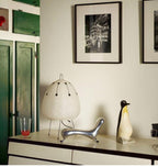 Decorative items on a shelf including a lamp, chair, and penguin figure with framed pictures on the wall.