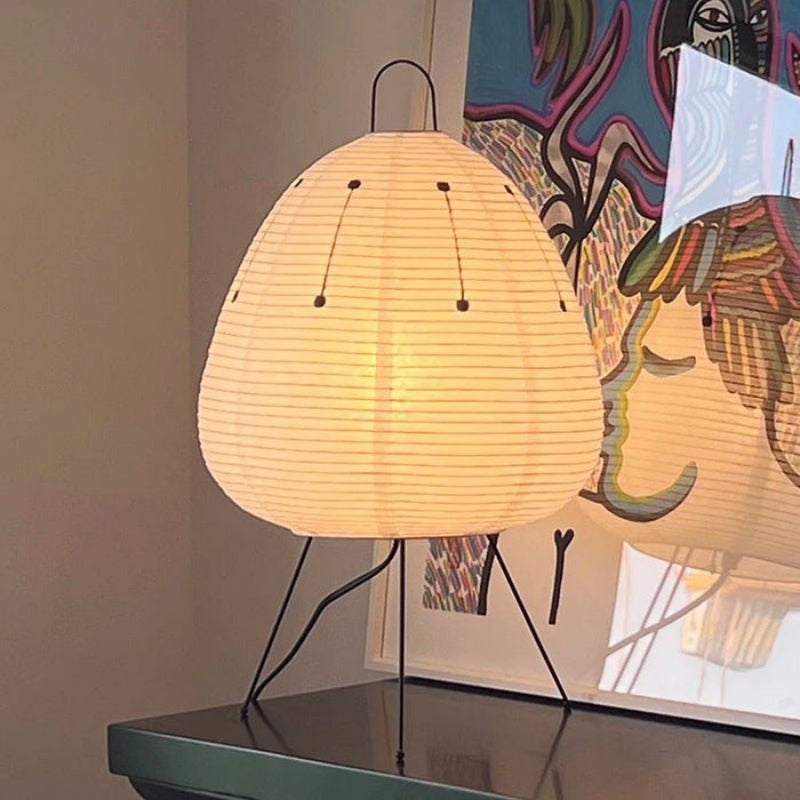 Table lamp with a woven shade on a surface, with colorful abstract art in the background.