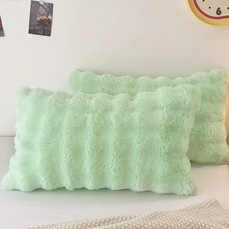 Two mint green fluffy rectangular throw pillows with scalloped edges, displayed on a white surface against a white wall.